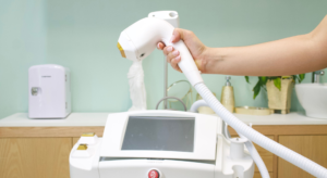 Medical laser device with a white handpiece held by a person's hand, connected to a hose and touchscreen panel in a clinic setting