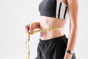 Person measuring their slim waist with a yellow measuring tape, wearing a sports bra and black shorts.